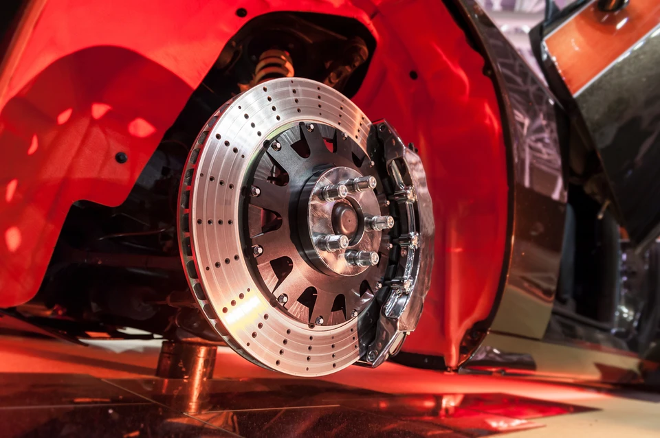 Atelier automobile avec véhicule rouge surélevé, roue démontée exposant le système de freinage