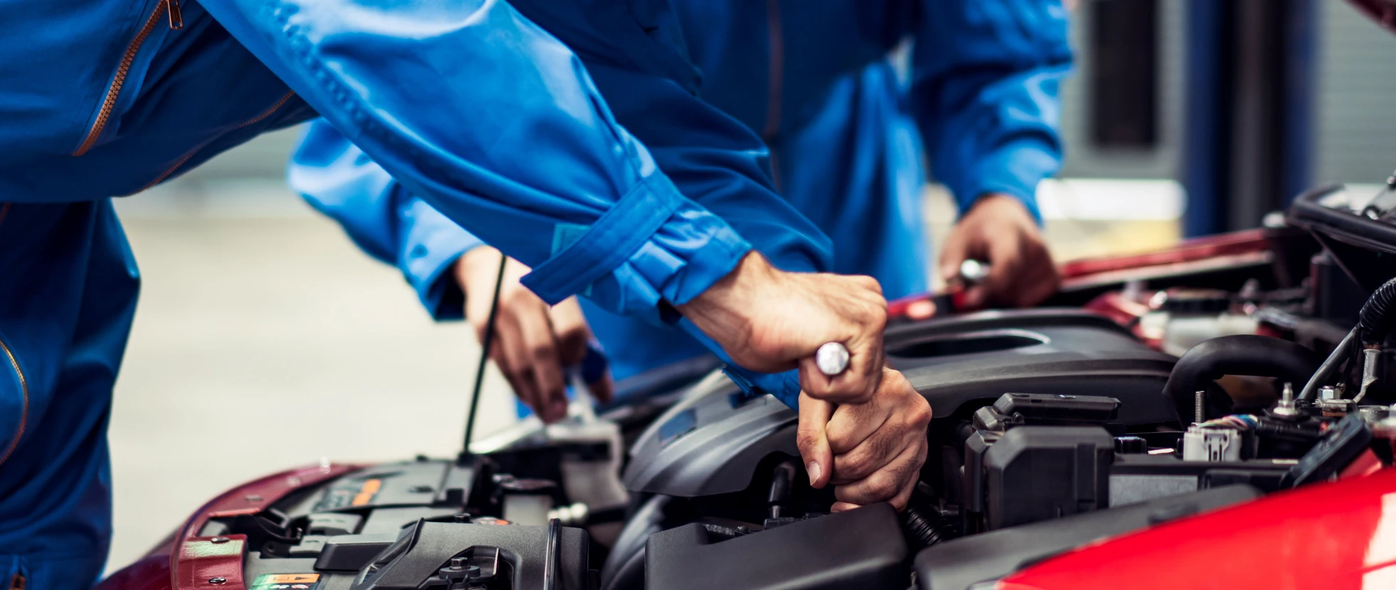 Mécanicien automobile en combinaison bleue effectuant une maintenance sous le capot ouvert d'un véhicule rouge dans un garage professionnel