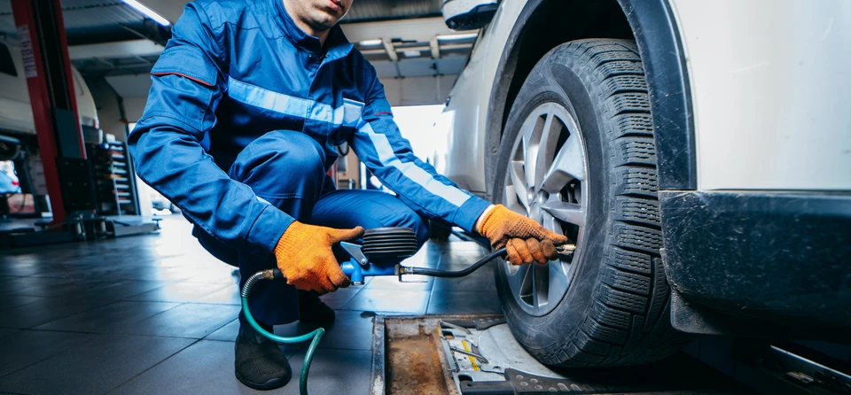 Des mains de mécanicien auto vérifient la pression d'air dans le pneu avant le réglage de la suspension et l'alignement des roues de l'automobile au poste de réparation