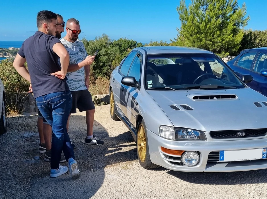 Rangée de véhicules neufs alignés sur parking pavé extérieur sous ciel nuageux