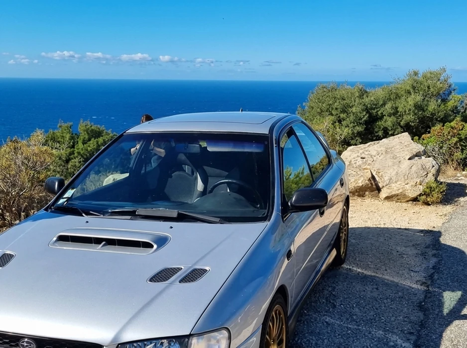 Voiture de sport compacte grise métallisée garée sur une route côtière avec vue panoramique sur la mer Méditerranée