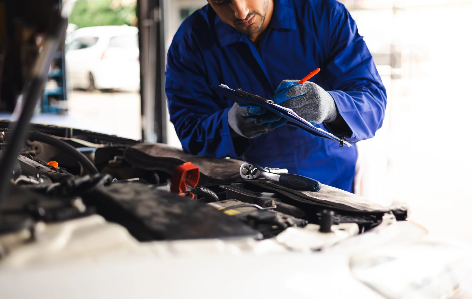Main d'un mécanicien automobile portant des gants de protection noirs tenant un filtre à huile neuf au-dessus du compartiment moteur d'un véhicule lors d'une opération de maintenance