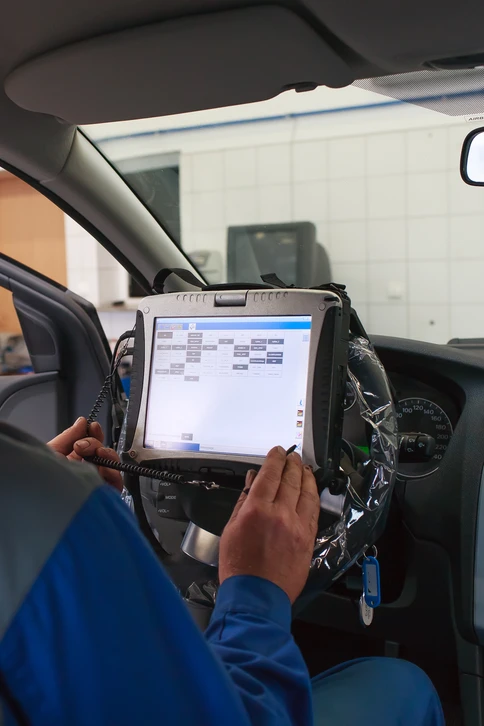 Mécanicien automobile dans atelier professionnel effectuant diagnostic électronique sur véhicule, capot ouvert, connecté à station de diagnostic verte
