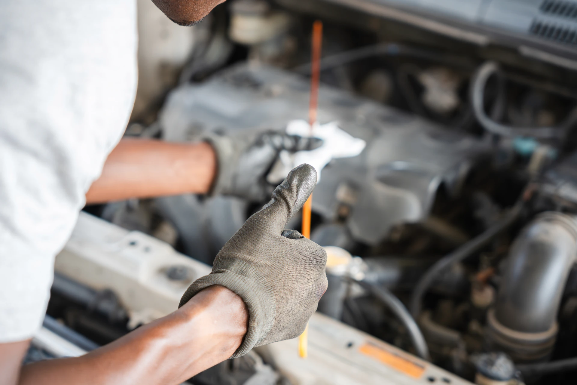 Mécanicien automobile en combinaison bleue effectuant une maintenance sous le capot ouvert d'un véhicule rouge dans un garage professionnel